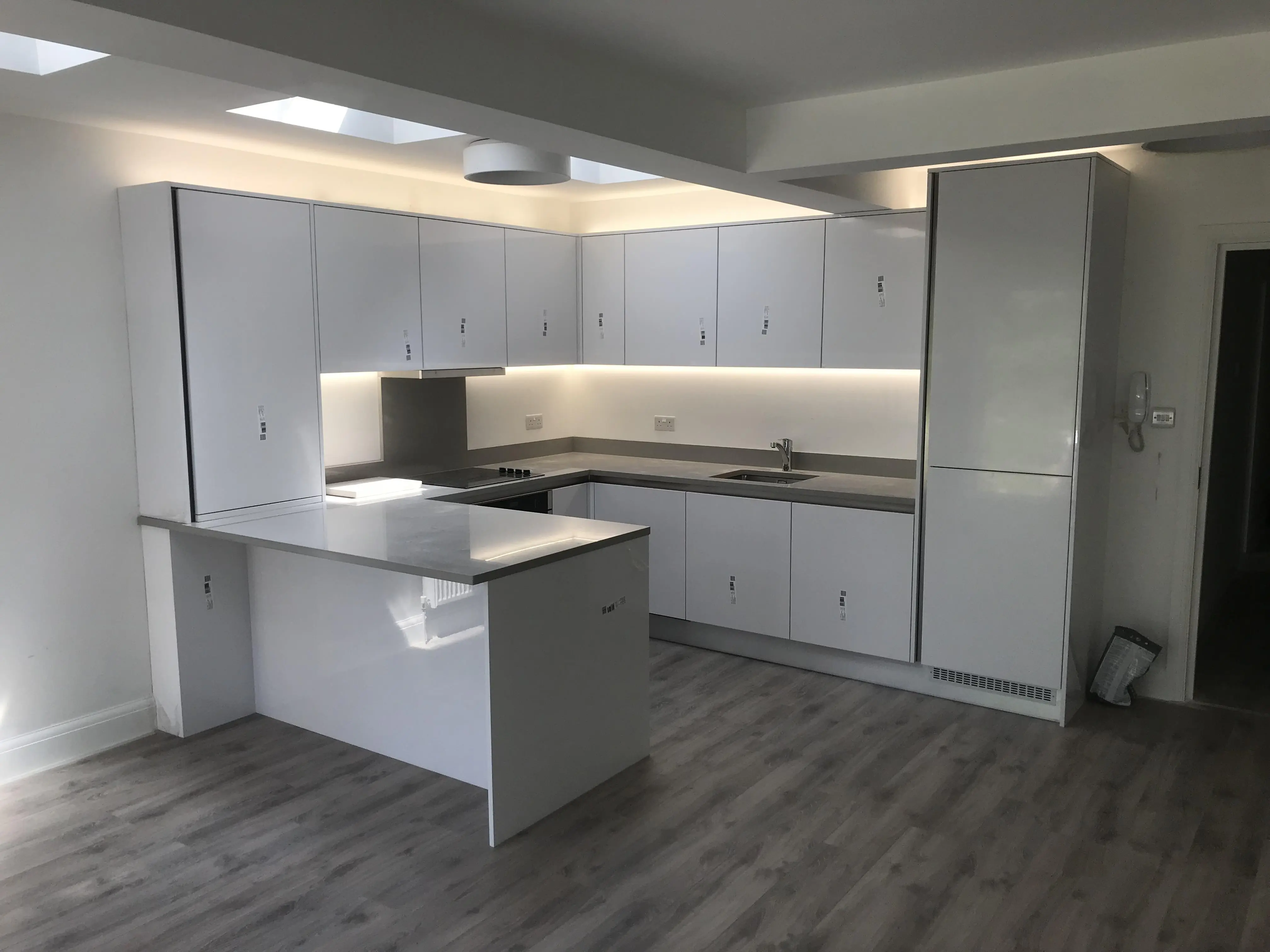 Magas fényű fehér (gloss white) konyha egy kertvárosi környezetben. Beépített gépek, gránit munkalap, rejtett LED fények jellemzik. Kilincs mentes kialakításával letisztult, modern megjelenést kaptunk.