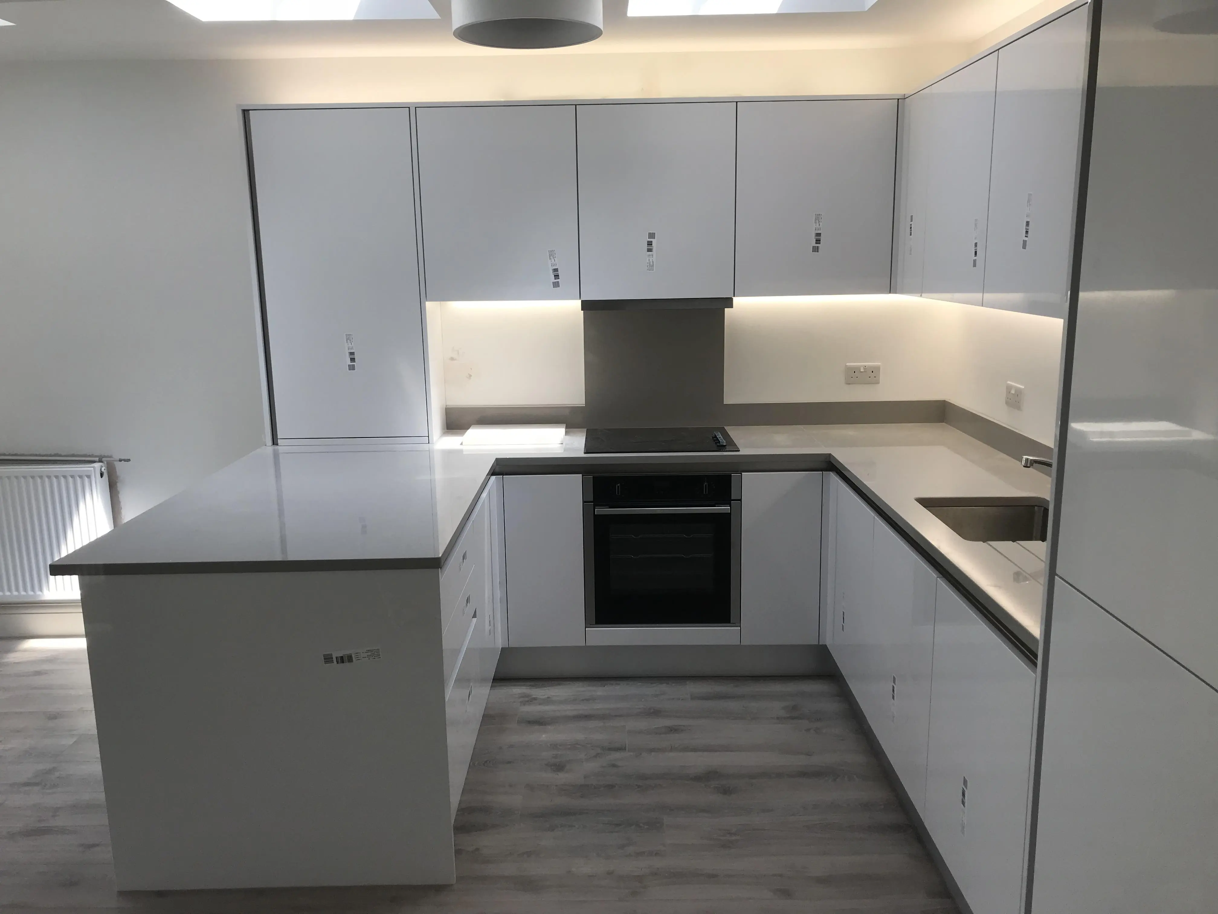 Magas fényű fehér (gloss white) konyha egy kertvárosi környezetben. Beépített gépek, gránit munkalap, rejtett LED fények jellemzik. Kilincs mentes kialakításával letisztult, modern megjelenést kaptunk.