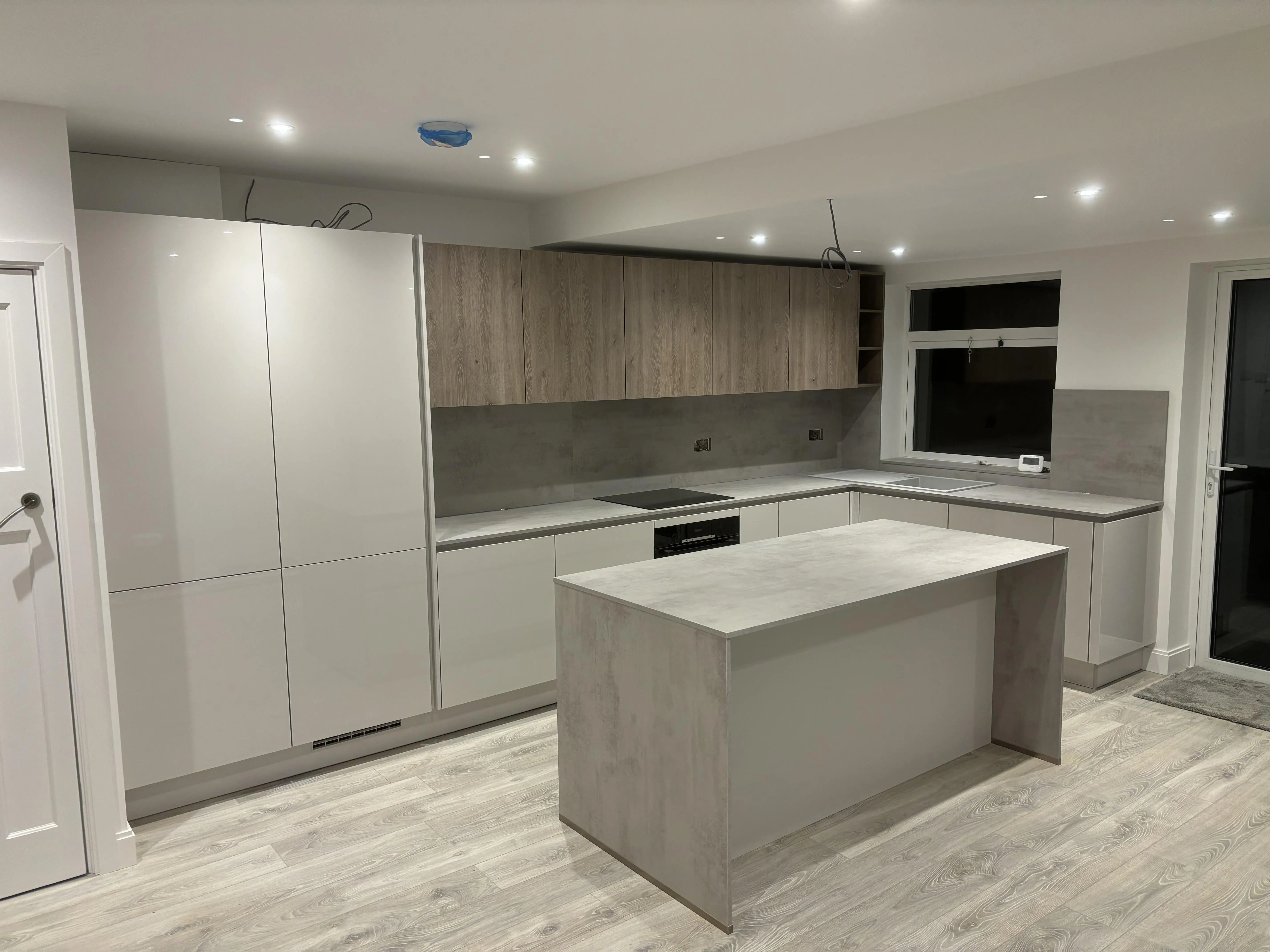 Kertvárosi ház letisztult konyhája. Teljesen gépesített, két színben megálmodott “L” alakú konyha szigettel. A munkapult 16 mm vastag, mely felfordul a hátfalra, és a sziget oldalát lezárja.