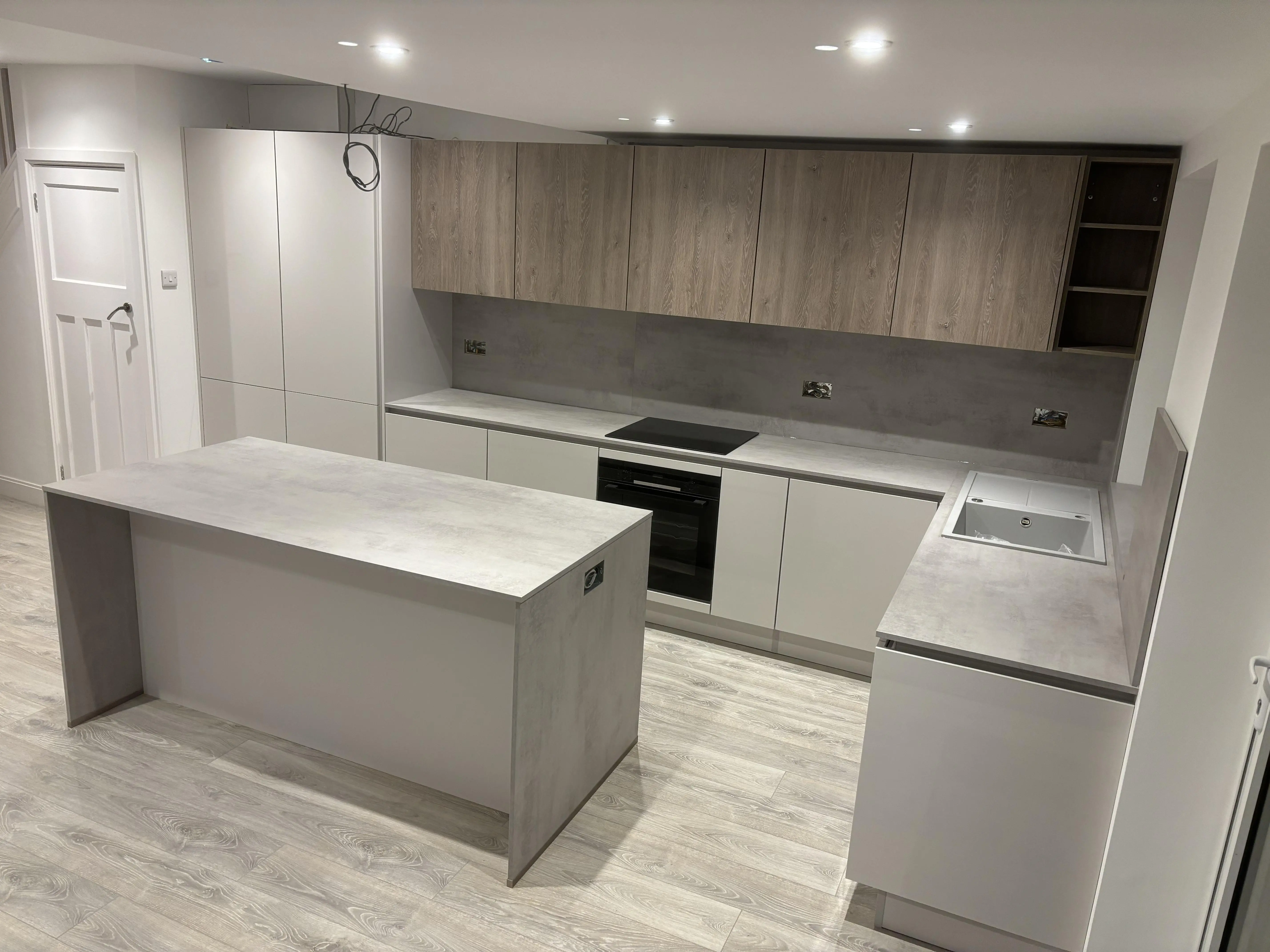 Kertvárosi ház letisztult konyhája. Teljesen gépesített, két színben megálmodott “L” alakú konyha szigettel. A munkapult 16 mm vastag, mely felfordul a hátfalra, és a sziget oldalát lezárja.