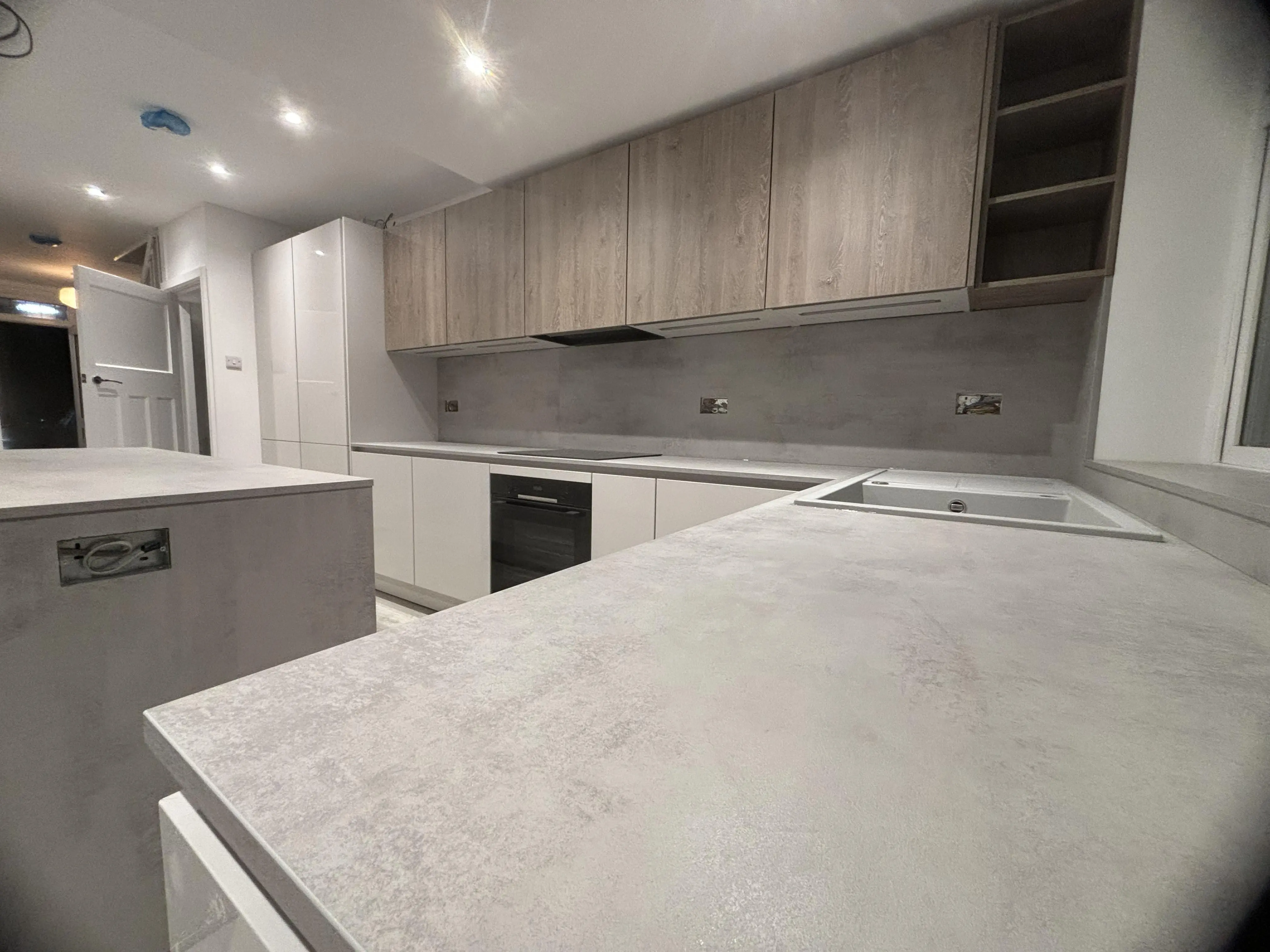 Kertvárosi ház letisztult konyhája. Teljesen gépesített, két színben megálmodott “L” alakú konyha szigettel. A munkapult 16 mm vastag, mely felfordul a hátfalra, és a sziget oldalát lezárja.