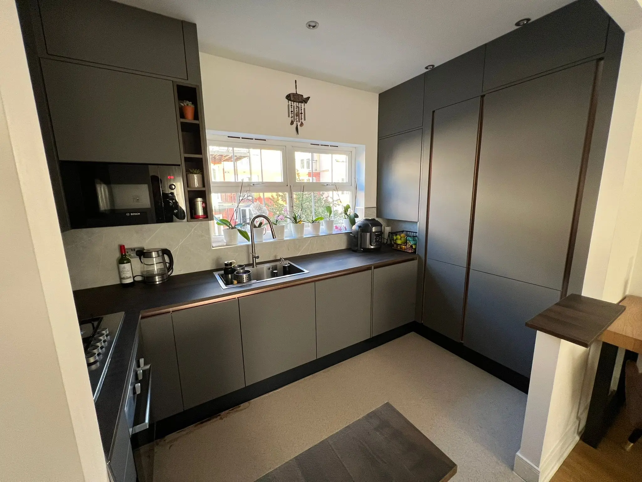 Társasházi lakás konyhája, matt antracit fronttal és kilincs mentes megoldásokkal. Extra szekrények a felső sorban hogy a mennyezetig fel legyen zárva. 25 mm vastag munkalap, teljesen gépesítve.